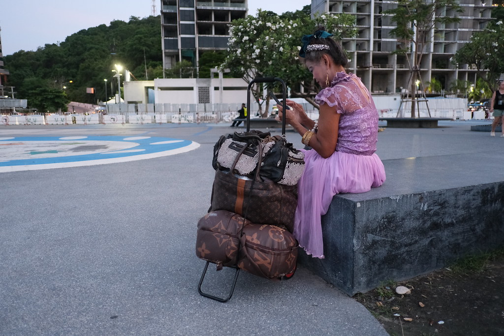 A woman sitting by a window at dusk, holding her phone and hesitating before replying to a message